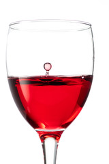 Splash from a drop of falling red wine to the surface in a round glass on a white background