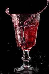 Splash of falling red wine in a round glass on a black background