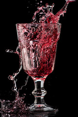 Splash of falling red wine in a round glass on a black background
