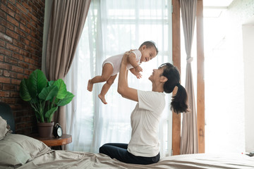 beautiful happy mother playing with her baby on the bed