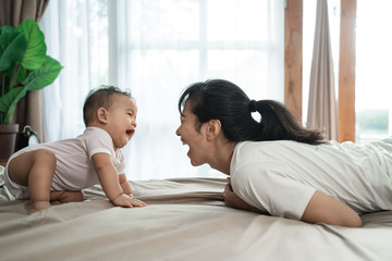 mother with baby playing on the bed in the morning