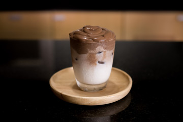 Iced Dalgona Cocoa / Chocolate, a creamy whipped cocoa, on wooden tray on black table. 