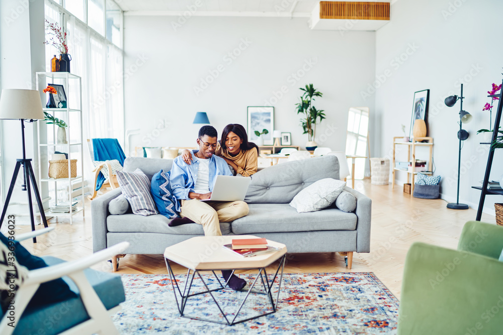 Wall mural Ethnic couple browsing laptop on sofa