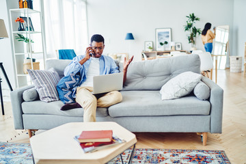 Puzzled male freelancer solving problem during teleworking on freelance checking web information on modern laptop computer and calling to customer service, African American man reading bad news