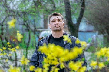 Portrait of brunette man, enjoying the view of spring yellow flowers on the street. 