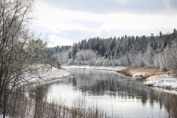 Countryside landscape view with river Venta flowing near beautiful snowy forest.