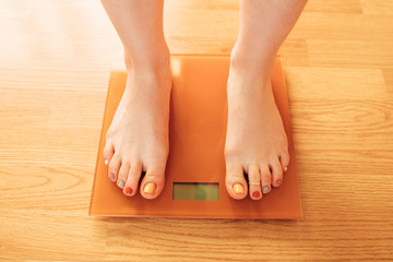 Caucasian woman feet standing on electic scales on home white wooden floor. Losing weight concept