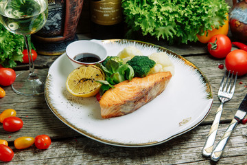 Restaurant dish with vegetable decor on a wooden background. Sea fish fried on a plate with sauce.