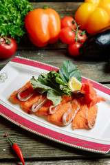 Restaurant dish with vegetable decor on a wooden background. Salted salmon cut into slices on a plate.