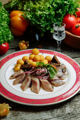 Restaurant dish with vegetable decor on a wooden background. Salted herring cut into slices on a plate.