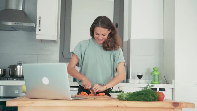 Young caucasian cheerful woman cooking in the bright kitchen while talking with friends via the internet. Cooking classes from a chef.