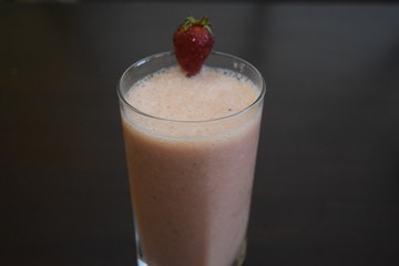 Closeup of strawberry smoothie with strawberry on top and brown background 