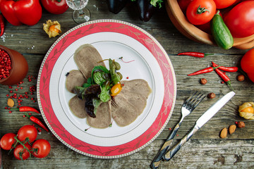 Restaurant dish with vegetable decor on a wooden background. Beef cut-up on a plate with greens.