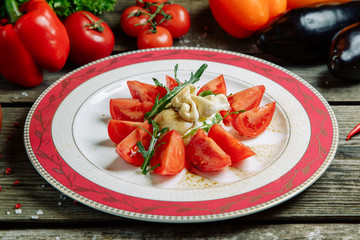 Restaurant dish with a decor of vegetables on a wooden background. Mozzarella cheese with tomatoes on a plate