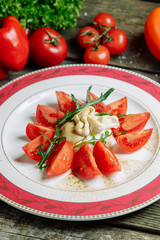 Restaurant dish with a decor of vegetables on a wooden background. Mozzarella cheese with tomatoes on a plate