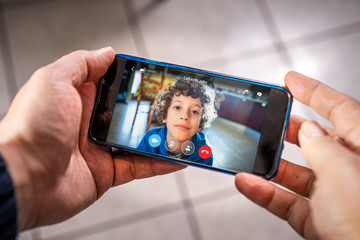 Father and son video calling with smartphone. Hands holding a smartphone with a child face.