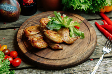 Restaurant dish with vegetable decor on a wooden background. Tobacco chicken with sauce and herbs on a plate.