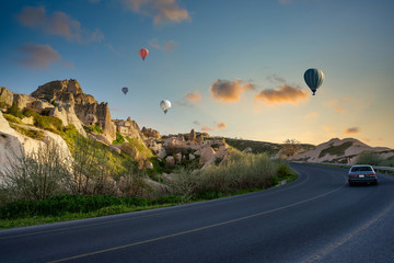 One car runs on the streets of the old town of Uchisar, a limestone mountain, with houses and balloons in the morning in Cappadocia. This is a popular tourist destination in Turkey.