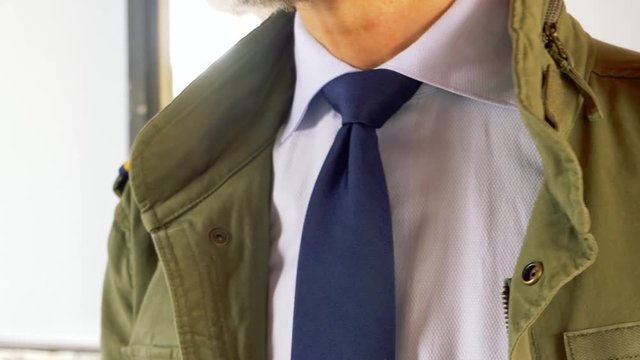 elegant man dressed in green jacket M65 and white pants. adjusts the knot of his blue tie
