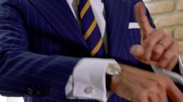 Elegant man dressed in blue pinstripe suit. shows us his cufflinks and his classic watch