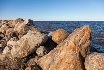 Fototapeta na wymiar Huge boulders covered with ice against the blue water of Lake Ladoga on a sunny day in early spring