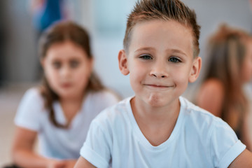 Portrait of a cute little boy in white t-shirt looking at camera and smiling while sitting on the floor in the dance studio