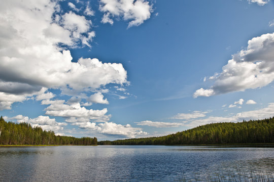 Beautiful volumetric clouds on a sunny day over a quiet forest lake