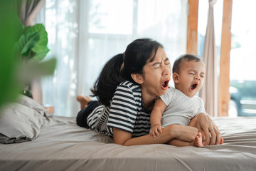 mother and child are yawning together while laying on the bed