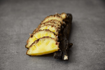 Slices of sweet ripe pineapple and eucalyptus branch on a gray stone surface. Close-up.