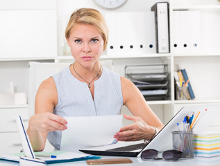 portrait of  woman working with documents and laptop and having problems at company office