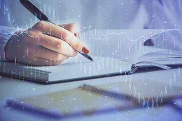 Multi exposure of woman's hands making notes with forex graph hologram. Concept stock market...