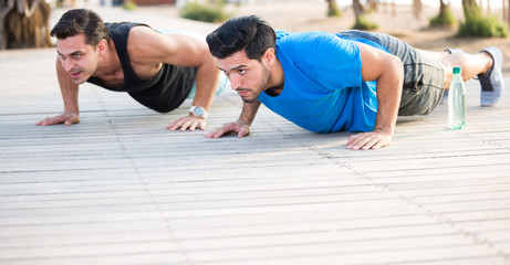 Obraz premium Smiling adult men are doing push-ups