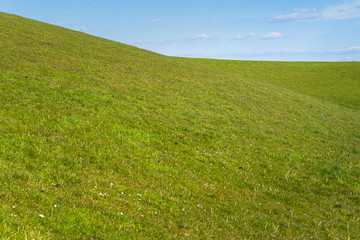 Green grass against blue sky with white clouds, Netherlands dike landscape along the Dutch coast