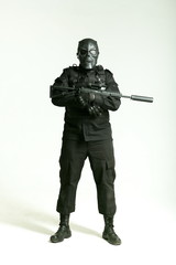 man in a black military uniform and full mask holding machine gun and standing full height on white background
