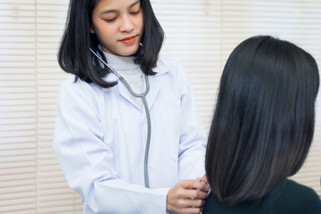 Young Asian female doctor uses the stethoscope to examine and diagnose adult female patient’s sickness and symptom. Medicine and health care concept. Doctor and patient.