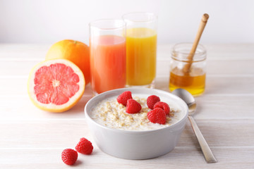 Oatmeal porridge with fresh raspberries in bowl on white wooden table. Healthy breakfast