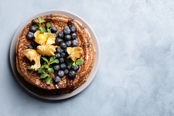 Cocoa Crepe Cake decorated with blueberries and physalis. Stack of thin pancakes with cream