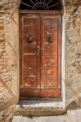 An old, rustic and weathered wooden door with cracked paint and rusty door knockers