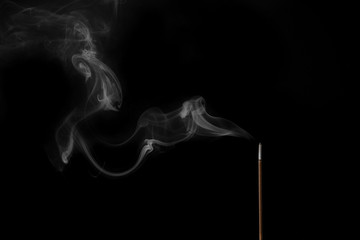 Incense stick smokes on a black background