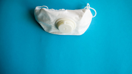 White protective medical mask with a valve on a blue background with copy space. Protective face mask against pollution, viruses, flu and coronavirus. Health care and surgical concept.