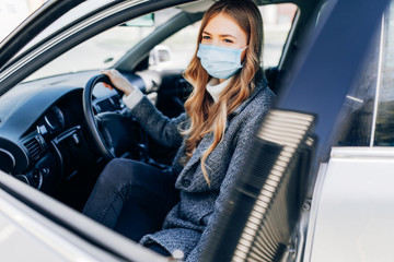 Beautiful young girl in a mask sitting in a car, protective mask against coronavirus, driver on a city street during a coronavirus outbreak