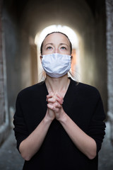 Coronavirus outbreak. Young caucasian woman wearing medical protection face mask praying over...