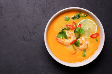 Tom Yam kung Spicy Thai soup with shrimp, coconut milk and chili pepper in bowl. Black stone background