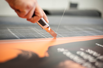 Close-up of hand with skalpel. Worker cut paper in printshop