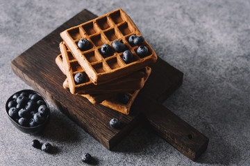 Belgian waffles with blueberries on cutting board. Traditional breakfast pastries