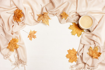 Top view of cup coffee cappuccino with milk foam,  warm fabric scarf, yellow autumnal season leaves of maple tree on white wooden table with copy space. Time for relax.