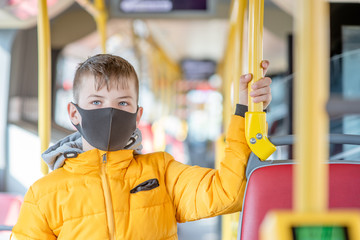 Boy wearing protective mask stand in the bus and holds on to the handrail