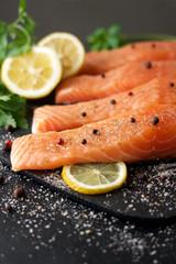 Salmon fillet with spices and lemons on black cutting board 