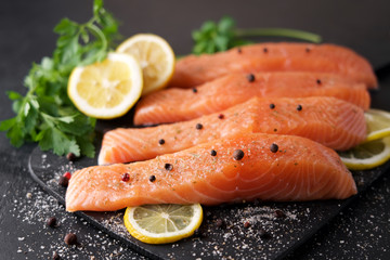 Salmon fillet with spices and lemons on black cutting board 