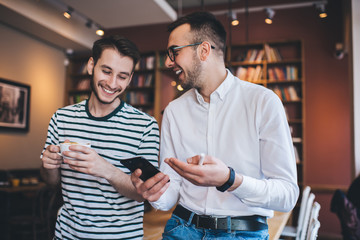 Excited men browsing smartphone in library